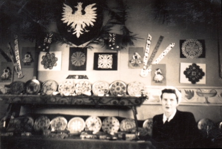 Mrs Kalinska, in a headscarf, in front of several dozen pieces of Polish craftwork.