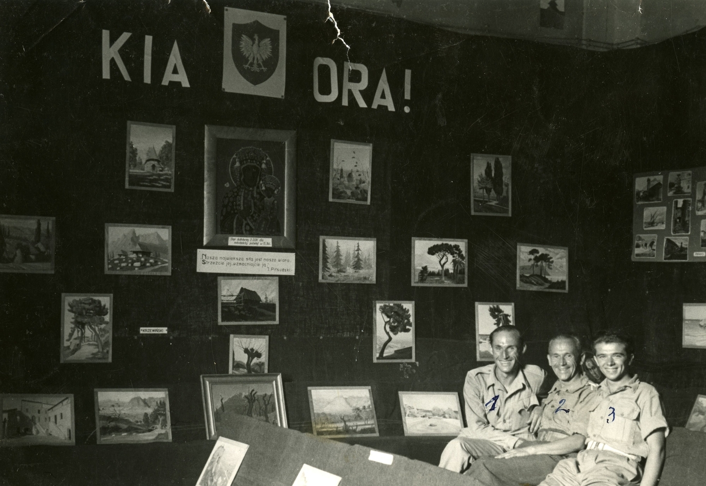 The three soldiers, in khaki, smiling at the camera in the right foreground, surrounded by paintings.
