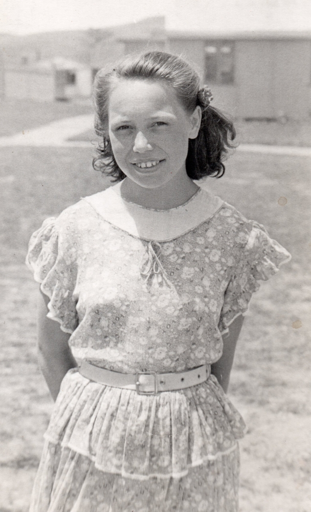 Henia 
Aulich standing in a summer dress, outside, in Pahiatua. Barracks in background