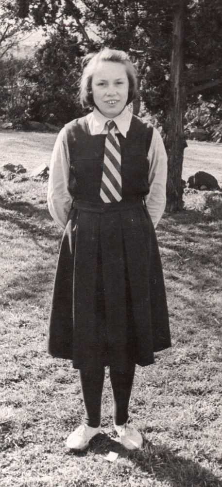 Henia in 
school gymslip, white shirt and tie standing in the school gardens