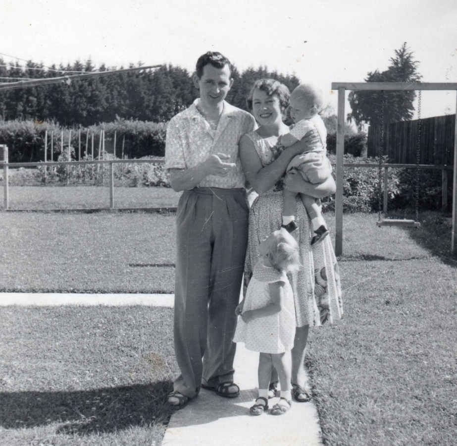 The young family 
in the gardene on a sunny day. Halina is carrying the toddler Gary and Christine, about three, is looking up at her father