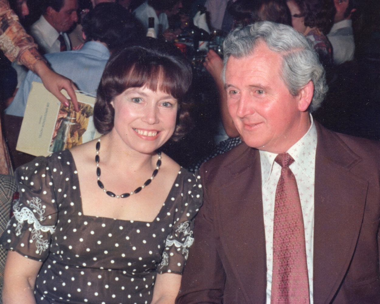 Henia and George 
at a social function. Henia's dress is brown-dotted, square-necked and has intricate lace detail on the short sleeves