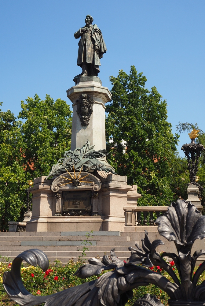 An imposing statue 
of the poet on a large plinth in a park-setting. In the foreground is a bit of the ornate metal fencing surround.