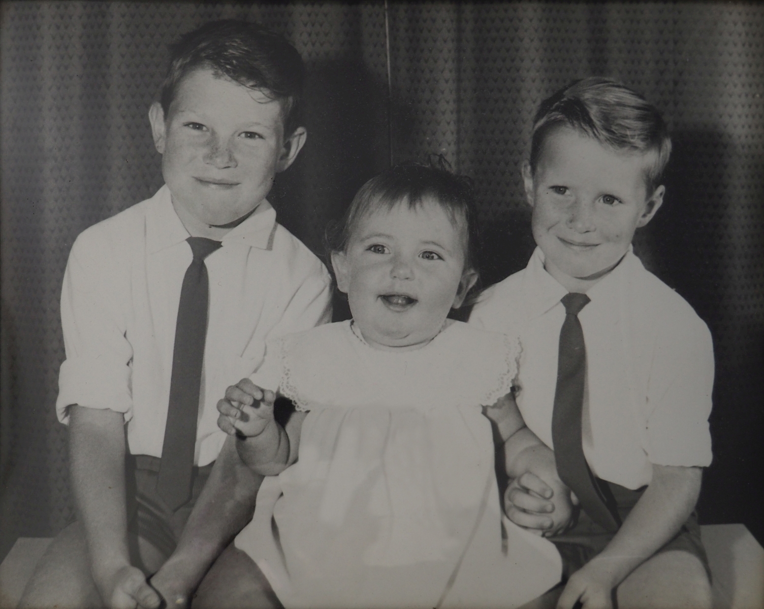 A black 
   and white studio photograph of the two older boys with their sister in the middle.