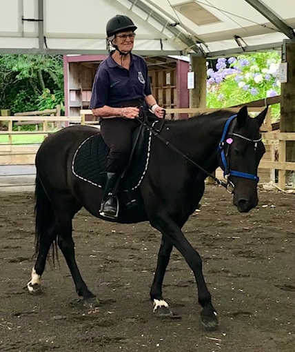 Faye, smiling and 
   looking comfortable on a black mare in an arena.