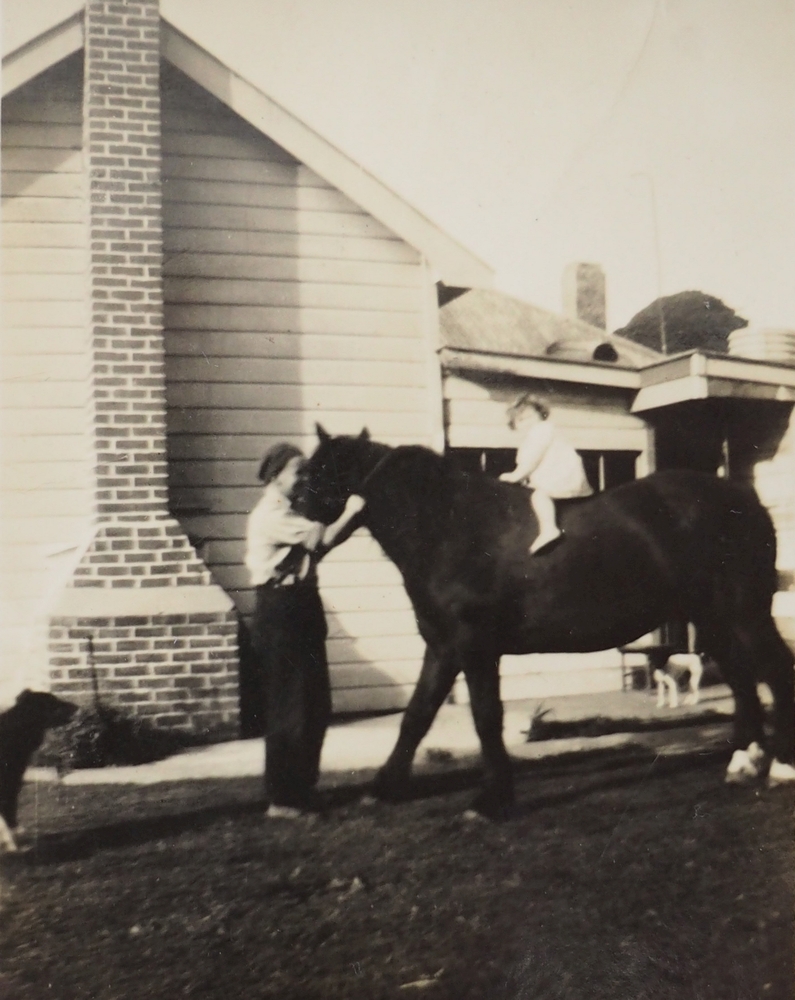 A black and 
   white photograph of a litle girl on a horse, with a man holding the horse's bridle.
