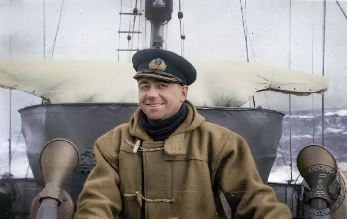 A charming shot of the  
commander on the deck of his ship. He is dressed in a heavy khaki duffle coat and smiling at the camera