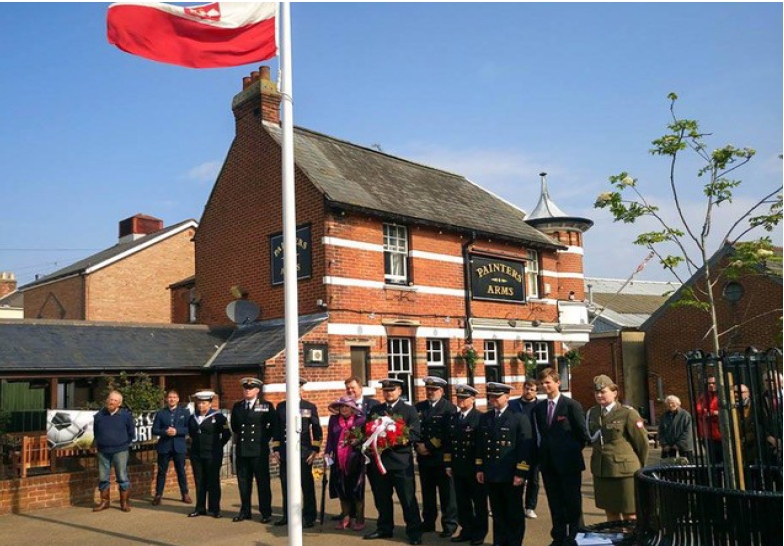 A group of people outside 
the Painters Arms at a flagpole which is flying the Polish flag. Most of the people are in naval uniform. A lovely sunny 
day.