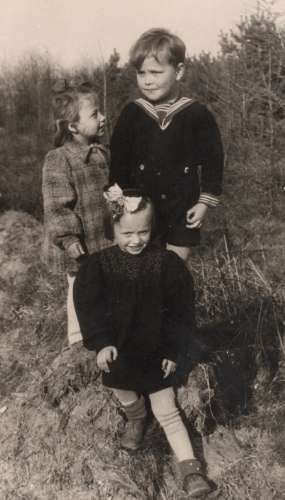 Three children 
perched on a rock with pine trees around them. Halina is looking up at the boy, and another little girl is sitting in front 
of them, on the rock