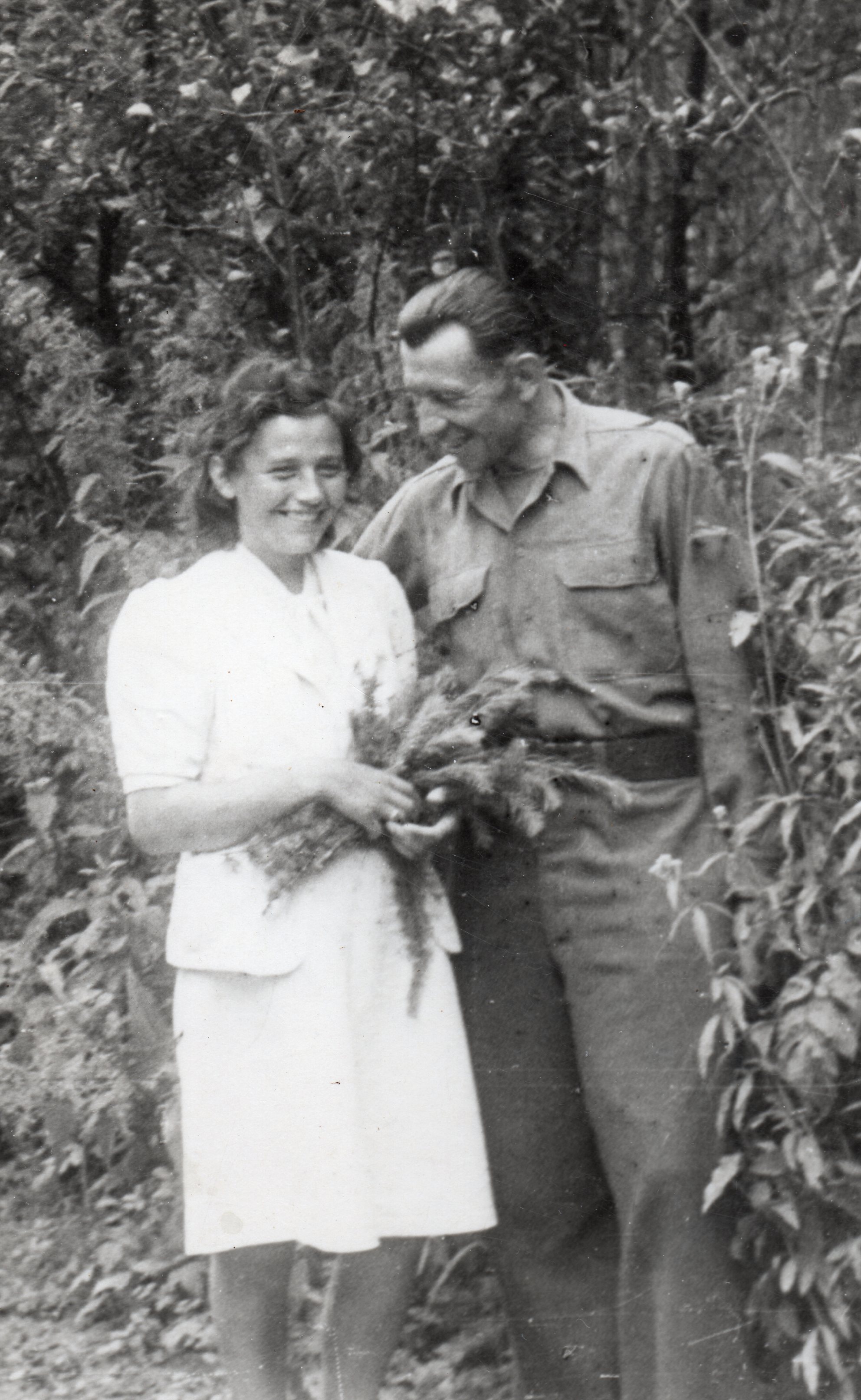 A black 
and white photo of Paweł in army fatigues, and Irena in a white suit. She has some greenery in her hands. Both are smiling 
widely and Paweł is looking down at Irena.