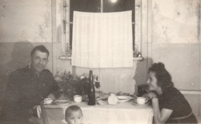 Paweł , in an army 
uniform, and Irena sit on either side of a laid table with a white cloth. Paweł  is looking at the camera and Irena is 
smiling at him. Halina's head just visible at the bottom.