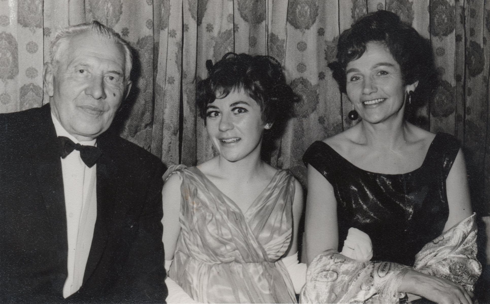 A black and white 
photo of the family, Hania in the middle of her parents, all dressed in formal attire.