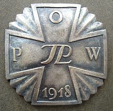 A burnished POW cross, 
lying on a background the same colour