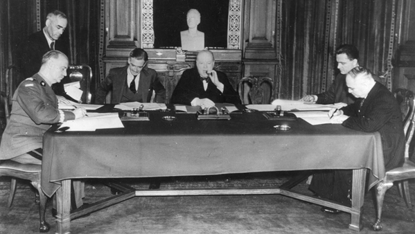 A black and white 
shot of five seated men at a table. There is an unidentified man standing on Sikorski's left, and another unidentified man 
sitting on the other side of the camera to Maisky. All ezcept Churchill are looking down. Churchill is looking directly at 
the camera.