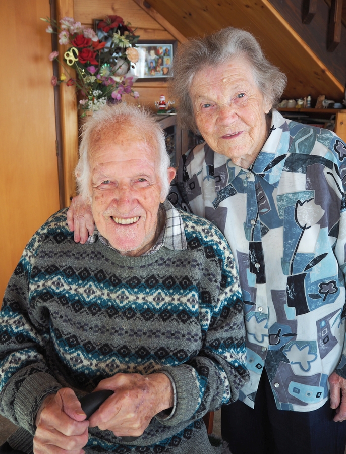 An inside, happy 
photograph of Zofia and Ken Derrick. Ken is sitting and Zofia is standing behind him with her hand on is shoulder.