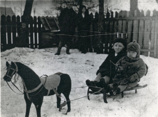 Jadzia and Jan 
Jarka on a sled in the garden with their parents in the background