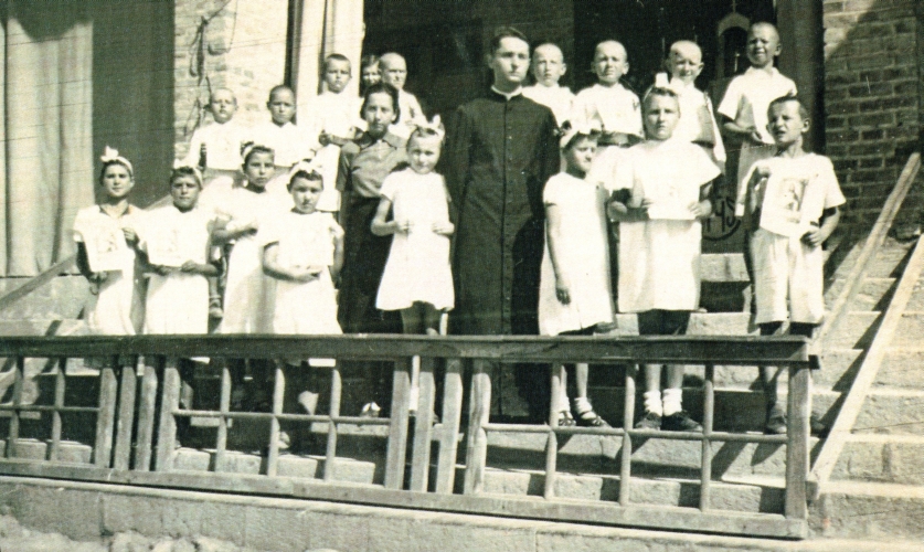 Group of 
children outside a church with priest