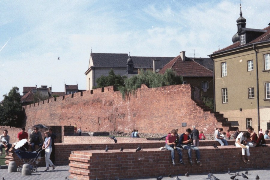 People sitting on 
the broken wall in Warsaw's Old Town, on a sunny day