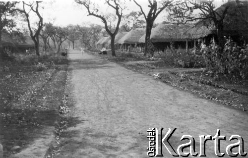 1945 black and 
white pic of a street in one of the Masindi camps, showing dirt road, thatched houses and trees