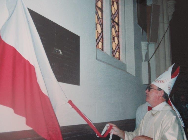 The bishop pulling away a 
Polish flag from the plaque