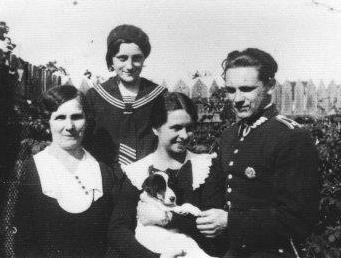 Black and white 
photograph taken outside. Danuta is in the middle holding a dog, Jozef in uniform but bare-headed on the right, his mother on 
the left and his sister at the back