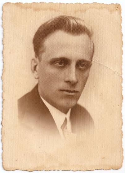 Studio head shot  
Józef Zając in a dark suit, looking away from the camera, serious expression, darkened deep-set eyes, photo fading below the 
tie-knot.