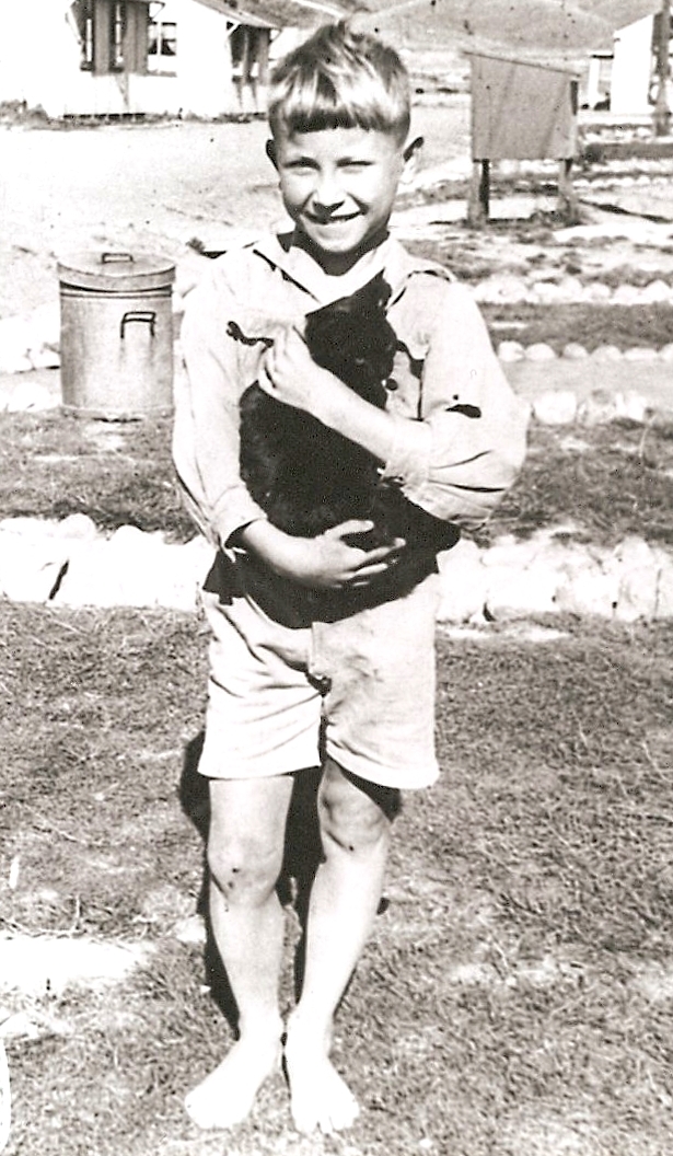Barefooted Kazik, in 
shorts and a long-sleeved white open-neck shirt, holds the placid black cat and beams.
