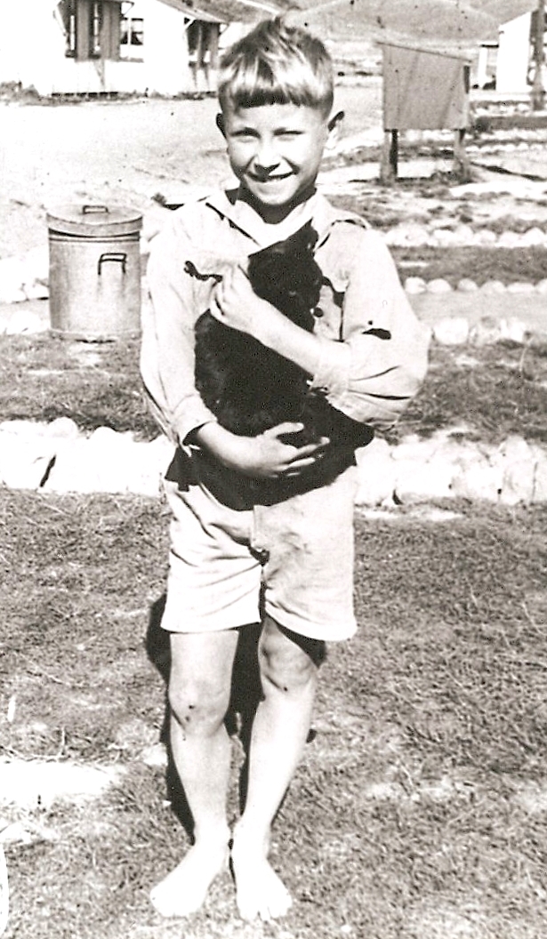 Barefooted Kazik, in 
shorts and a long-sleeved white open-neck shirt, holds the placid black cat and beams.