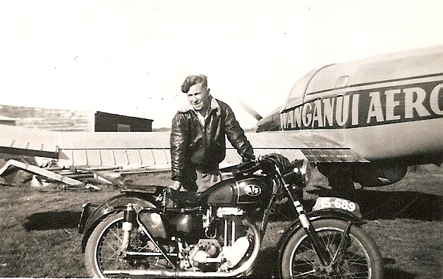 Kazik 
behind his motorbike, in leather jacket, and part of an aeroplane with Wanganui Aero written on the side.