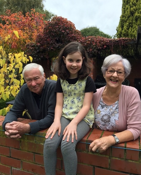 Kazik, Jan and 
their granddaughter, Lucy, in the garden, Lucy sitting on a wall.