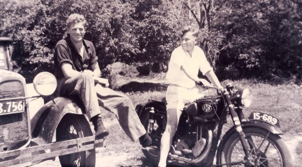 Kazik on his motorbike, 
smiling at Jan, who is sitting on the wheel-rim of his car.