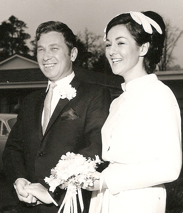 Head to thigh 
pic of Kazik and Jan after their wedding, both smiling widely, Jan with a flat, white head adornment and delicate posy, Kazik 
with hands clasped.