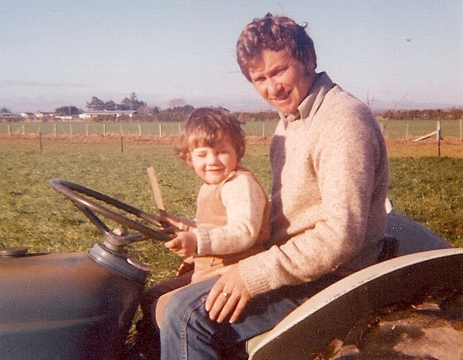 Kazik 
and Justin sitting on a tractor, dressed in jerseys, weather sunny.