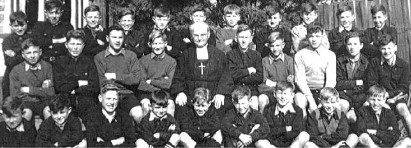 Casual school 
photo, taken outside, of some of the boys with a religious brother sitting in the centre