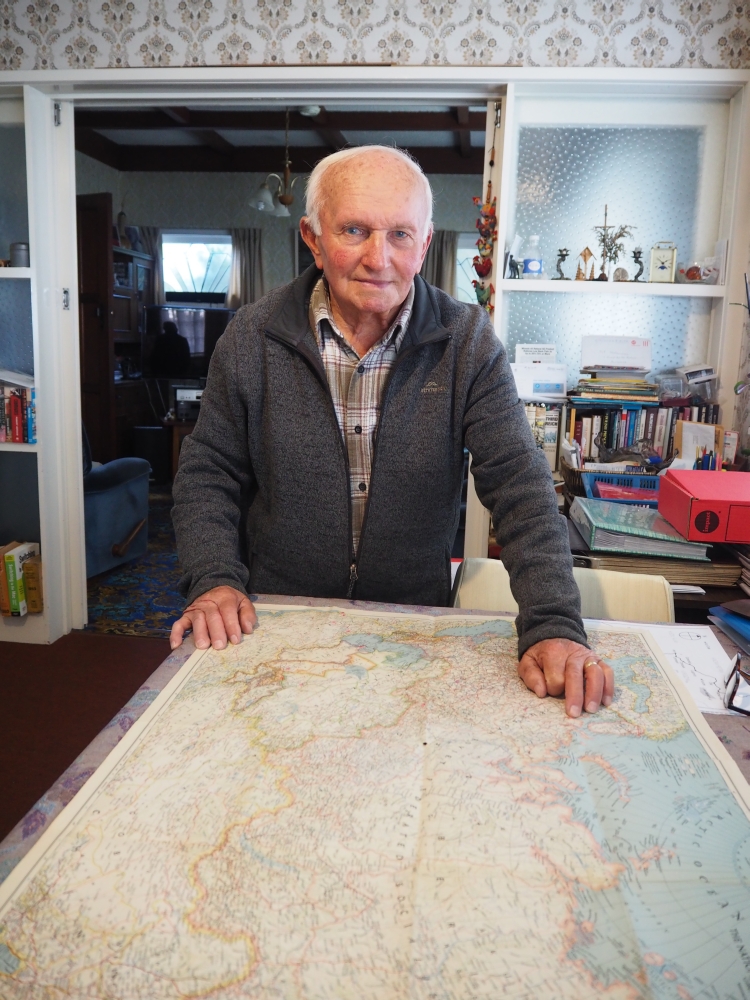 Jan Kaźmierów, in a 
grey sweater, standing at a table on which a map of the USSR lies.