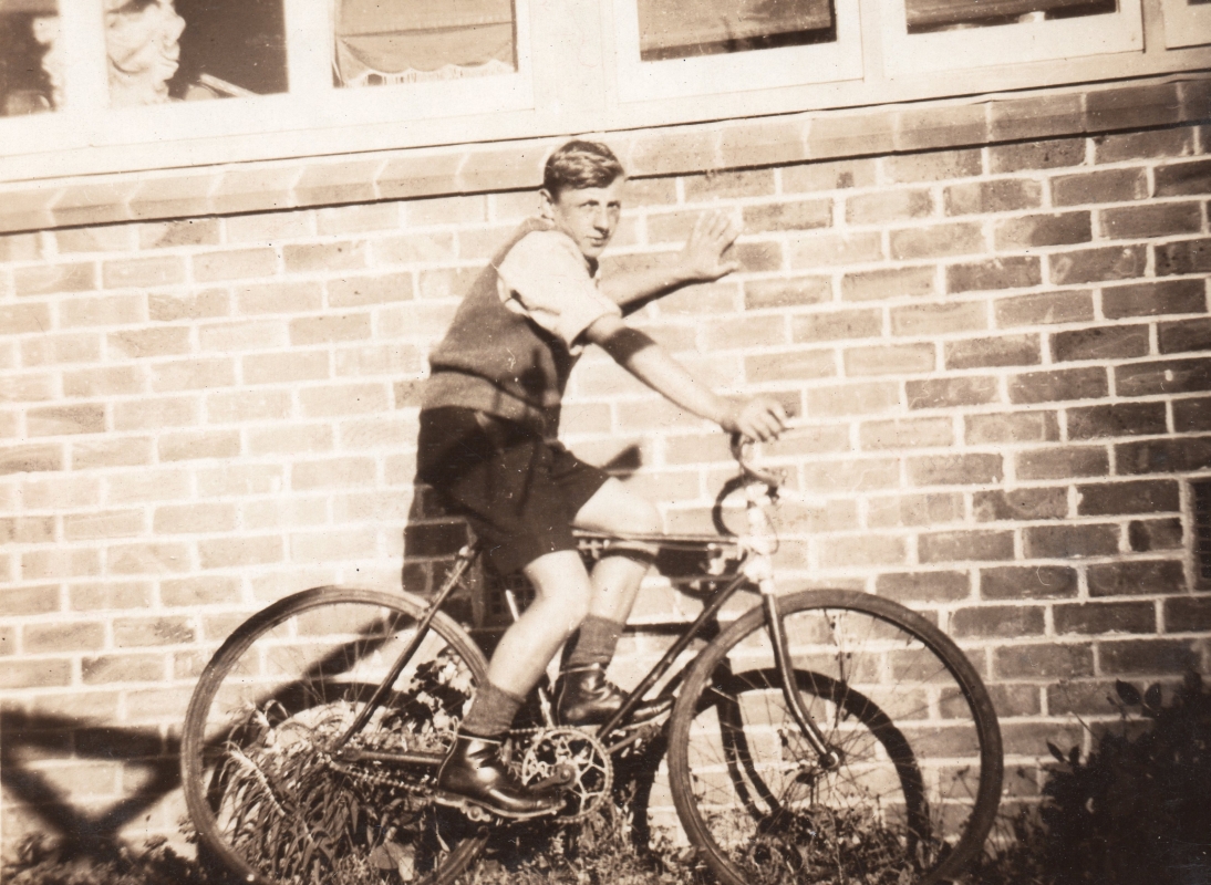 Black and 
white photograph of Tomasz, about 15, on his bike and leaning against the brick wall of a house.