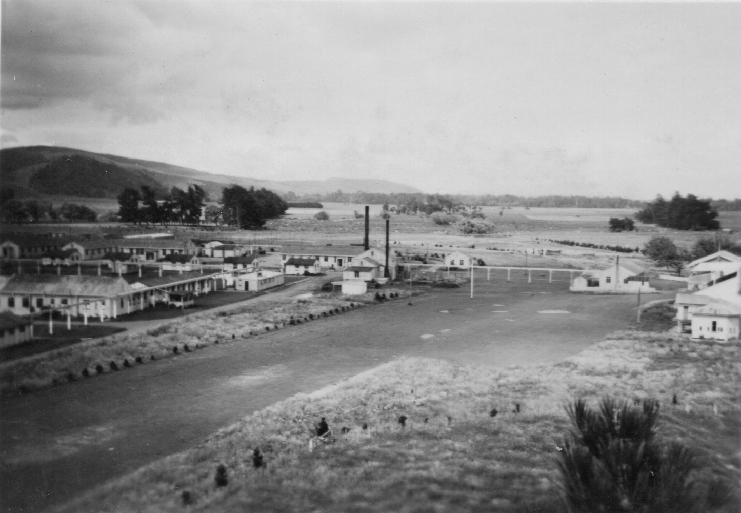 First of seven 
black and white photographs of the Pahiatua camp. This one shows the camp on both sides of the old racetrack, pre-fabricated 
buildings and hills in the background.