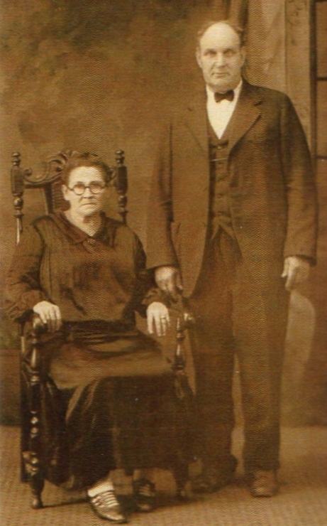 A 
blurry studio photo of Johann and Augustine. He is standing, she is seated in a large chair