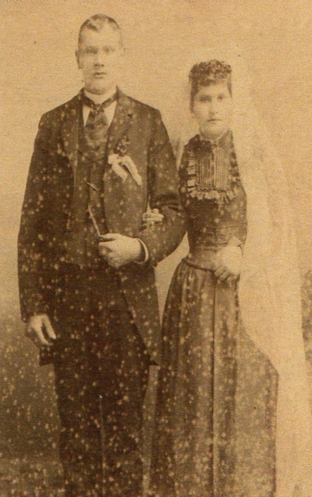 A 
blurry studio photo of Johann and Augustine standing in dark formal attire. Augustine has a long white veil.