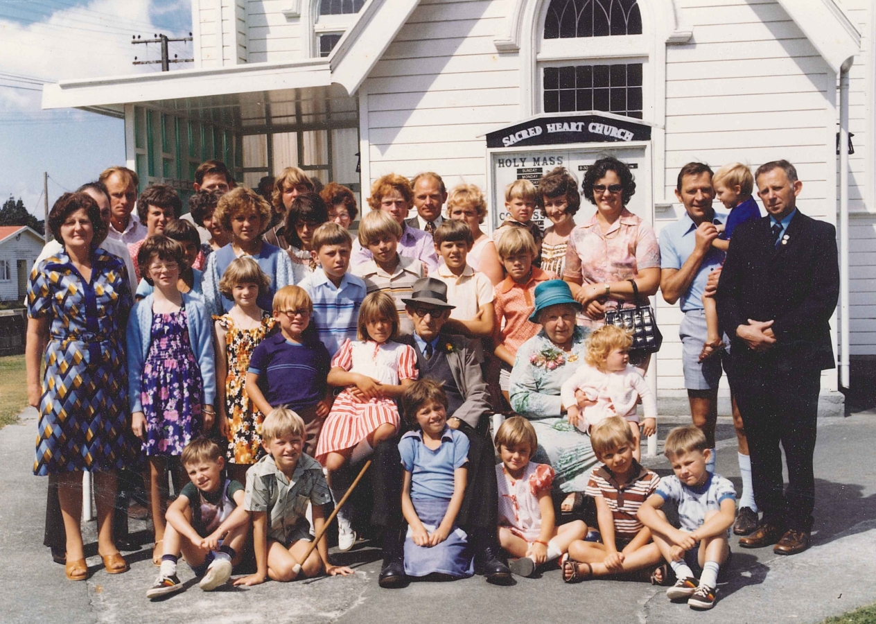 Coloured informal group photograph of Jacob and Ellen surrounded by their large family. Both Jacob and Ellen have 
children on their laps. This time, Ellen smiling. A lovely sunny day.