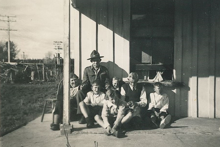 Black and white 
photograph of Ellen and Jacob with their boys on the veranda of their Inglewood house. Joe is sitting on a chair but all the 
rest are sitting on the floor. There is a chair behind Ellen, so she did not give her seat up for Joe. Jacob is looking down, 
the sash window behind open about 30cm and a curtain coming out.