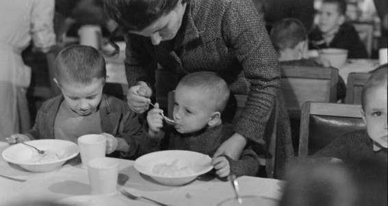 Three Polish  
boys at a dining table, woman helping middle one to eat