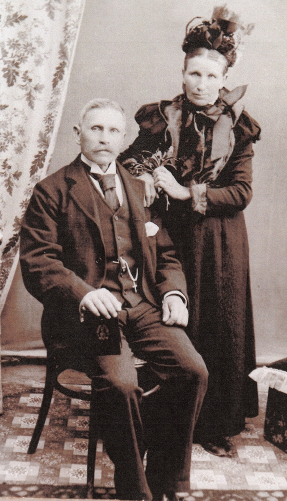 A formal studio photograph of Michael Francis and Cecelia, Michael sitting, his hand on a picture of Our Lady, Cecelia 
standing behind, hand her husband's shoulder and holding a posie of flowers in the other.