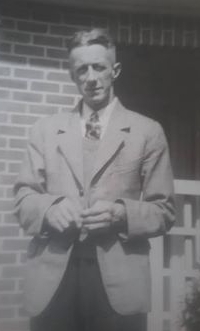 A blurred shot of Alfred in 
a light jacket, dark trousers and tie taken outside a house.