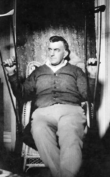 A grumpy-looking 
Herbert, not looking at the camera, sitting with crutches