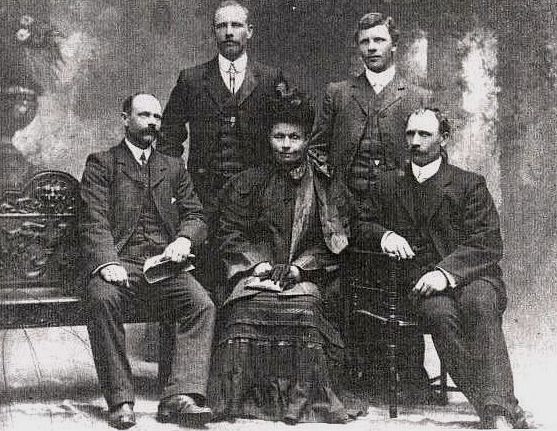 A studio photograph 
of Franciszka, seated, and surrounded by her sons. All are in formal atttire and she is wearing a hat and holding gloves