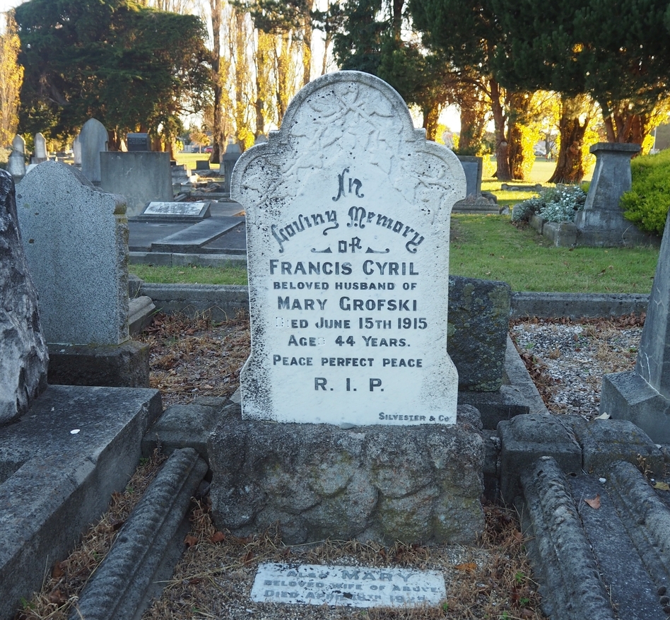 Headstone of 
Francis Grofski, with Mary's addition at his feet. The cleaned headstone stands among others in the shade, but the background 
is a setting sun through the trees.