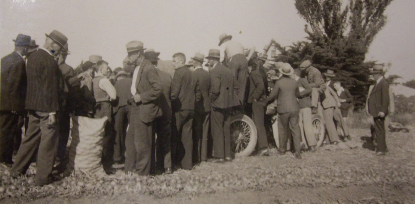 Group of men 
surround a hidden machine, presumably an example bag to the left.