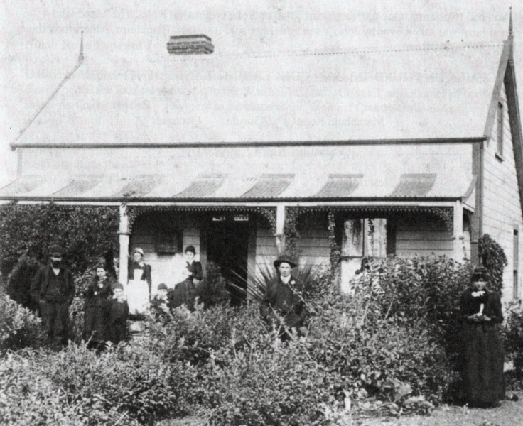 Christopher and Louisa Schimanski, outside their house with several members of their family. Sunday best clothes, and a 
garden of shrubs. Filigree details around the veranda pillars.