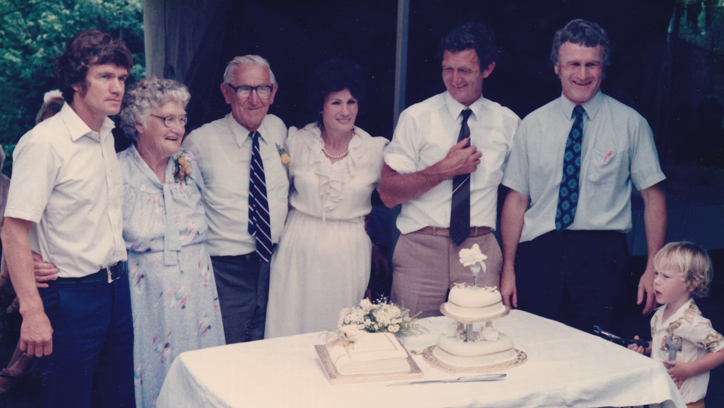 Adult children and parents behind a table with a white cloth and two anniversary cakes